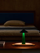 Green lamp on a wooden table with a bed in the background