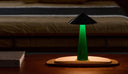 Green lamp with black shade on a wooden surface, blurred sofa in the background